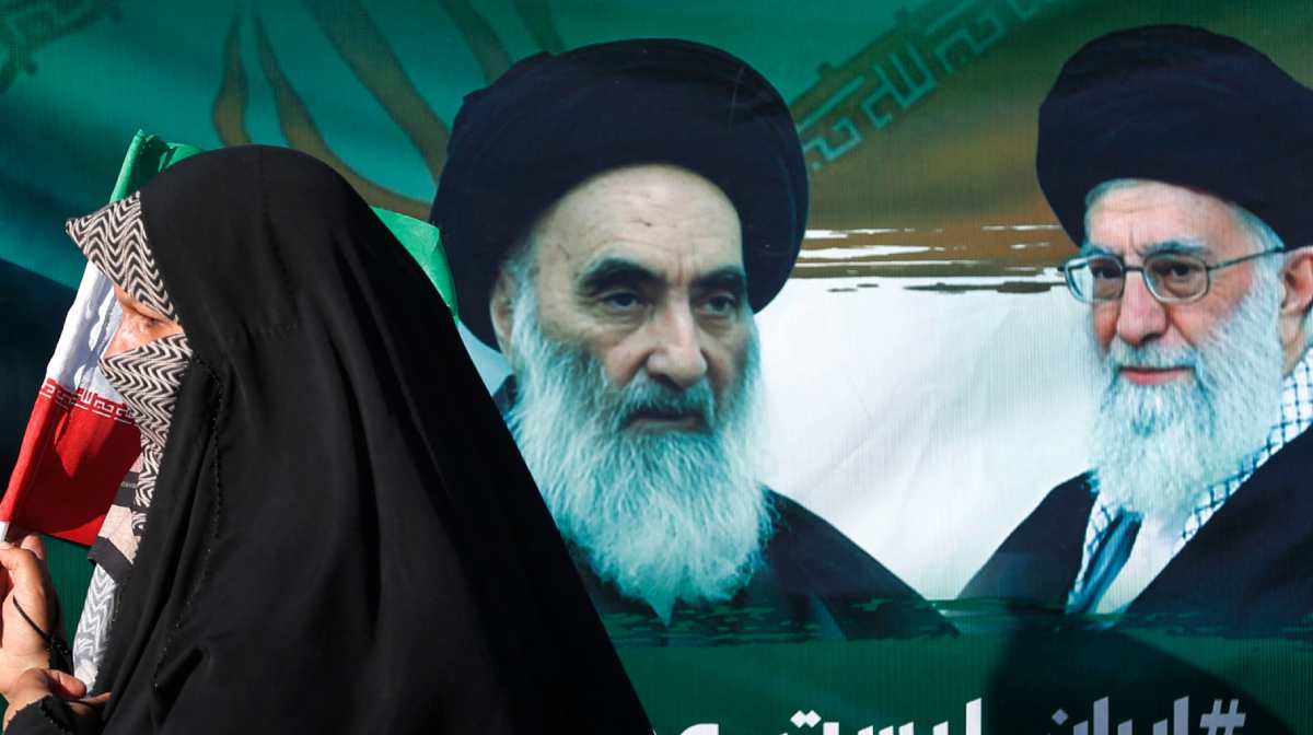 TOPSHOT - An Iraqi woman walks past a portrait of Iraq's top Shiite cleric Ayatollah Ali al-Sistani and Iran's supreme leader Ayatollah Ali Khamenei during march in the Kadhimiya district of Baghdad on June 21, 2025, to protest against Israel's strikes on Iran. (Photo by AHMAD AL-RUBAYE / AFP)