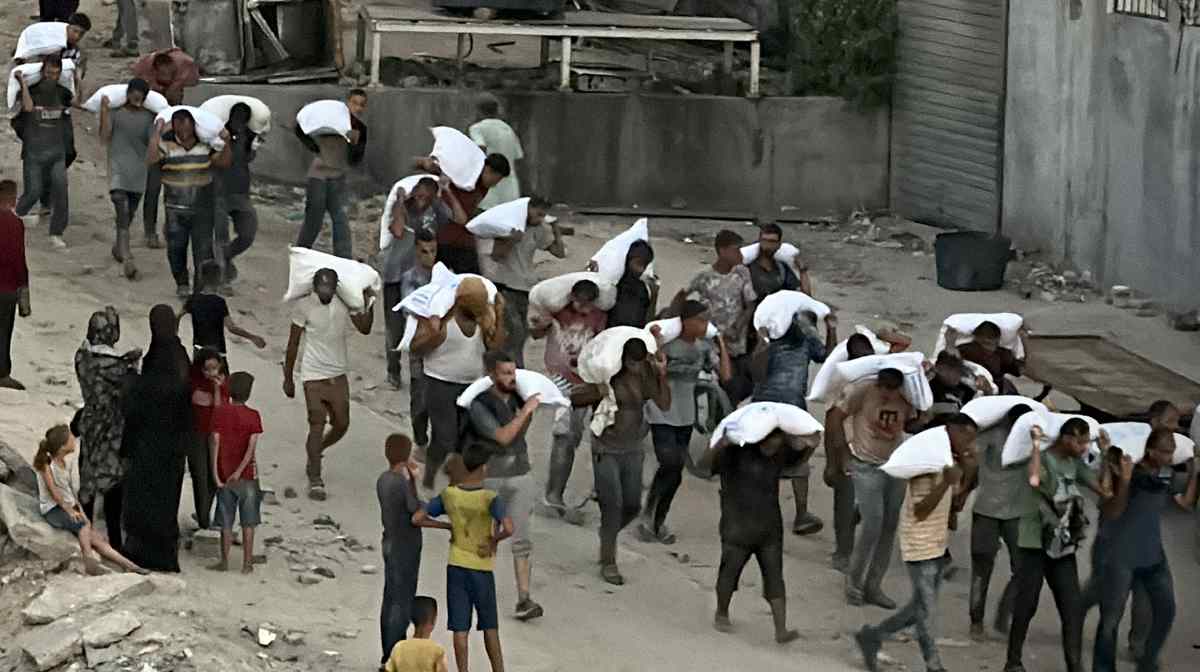  Men walk carrying sacks of flour that were taken from a raided truck carry sacks of flour after raiding a truck that was carrying foodstuffs, in Khan Yunis in the southern Gaza Strip on July 22, 2025. (Photo by AFP)