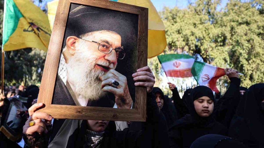 Iranian women married to Iraqis carry a portrait (L) of Iran's Supreme Leader Ayatollah Ali Khamenei and wave Iranian flags during a demonstration near the Iranian embassy in Baghdad on January 16, 2026, against Israel and recent US threats of military action in Iran, and in support of the Iranian regime and its supreme leader. (Photo by AHMAD AL-RUBAYE / AFP)