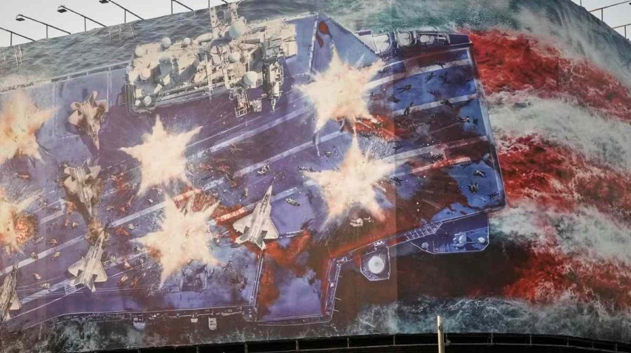 Vehicles drive past a billboard depicting a damaged U.S. aircraft carrier with disabled fighter jets on its deck and a sign reading in Farsi and English, "If you sow the wind, you'll reap the whirlwind," at Enqelab-e-Eslami (Islamic Revolution) Square in Tehran, Iran, Sunday, Jan. 25, 2026. (AP Photo/Vahid Salemi)