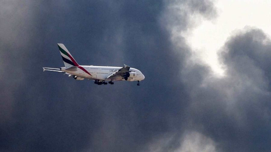 An Emirates Airbus A380 aircraft prepares for landing as a smoke plume rises from an ongoing fire near Dubai International Airport in Dubai on March 16, 2026. Flights were gradually resuming at Dubai airport on March 16, previously the world's busiest for international flights, the airport operator said, after a "drone-related incident" sparked a fuel tank fire nearby, as Iran kept up its Gulf attacks.