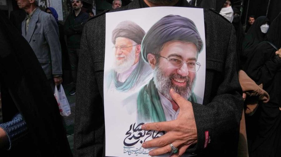 A mourner holds a poster depicting Ayatollah Mojtaba Khamenei, right, the successor to his late father Ayatollah Ali Khamenei, left, as supreme leader, during the funeral procession for senior Iranian military officials and civilians killed during the U.S.-Israel campaign in Tehran, Iran, March 11, 2026. (AP Photo/Vahid Salemi, File)