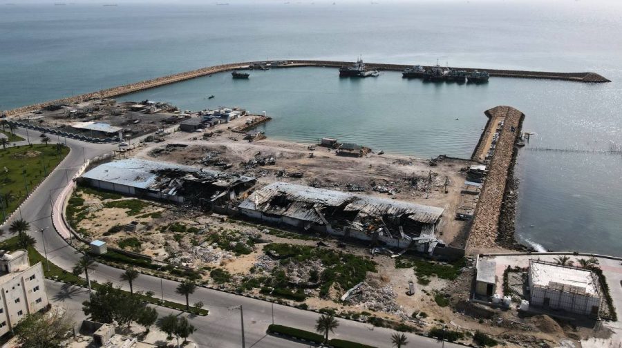 Backdropped by ships in the Strait of Hormuz, damage, according to local witnesses caused by several recent airstrikes during the U.S.-Israel military campaign, is seen on a fishing pier in the port of Qeshm island, Iran, Monday, April 13, 2026. (AP Photo/Asghar Besharati)
