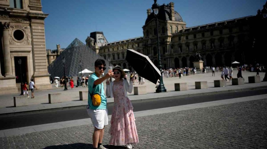 Tourists with an umbrella take a photo in Paris, as France is enduring a grueling heat wave with temperatures soaring above 40 degrees Celsius (104 Fahrenheit), Monday, June 22, 2026. (AP Photo/Christophe Ena )