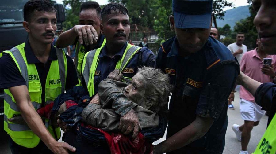 Rescuers carry in their arms a flood survivor, following flash floods and a landslide disaster in Devghat, in the Nepal's Nuwakot district on August 26, 2026. A massive flood and landslide disaster on the Nepal-Tibet border killed at least 103 people on August 26, 2026 and left several hundred missing, many of them foreign tourists. Aid workers said entire settlements had been "wiped out". Some 403 tourists -- 341 of them foreigners -- were unaccounted for several hours after the disaster struck, according to the tourism ministry. (Photo by PRAKASH MATHEMA / AFP)