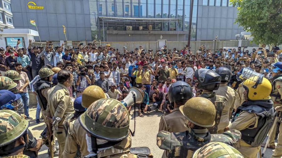 Security personnel stand guard as factory workers stage a protest demanding a hike in wages, in Noida, Gautam Buddh Nagar district, Uttar Pradesh, Monday, April 13, 2026. The protest carried incidents of arson, vandalism and stone-pelting reported from Phase-2 and Sector 60 areas, police said. (PTI Photo)(PTI04_13_2026_000100A)(PTI04_13_2026_000223B)