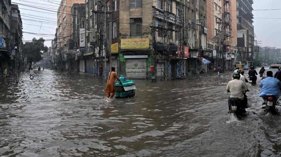 Commuters wade through a flooded street after heavy rainfall in Lahore on July 25, 2026. (Photo by Arif ALI / AFP)
