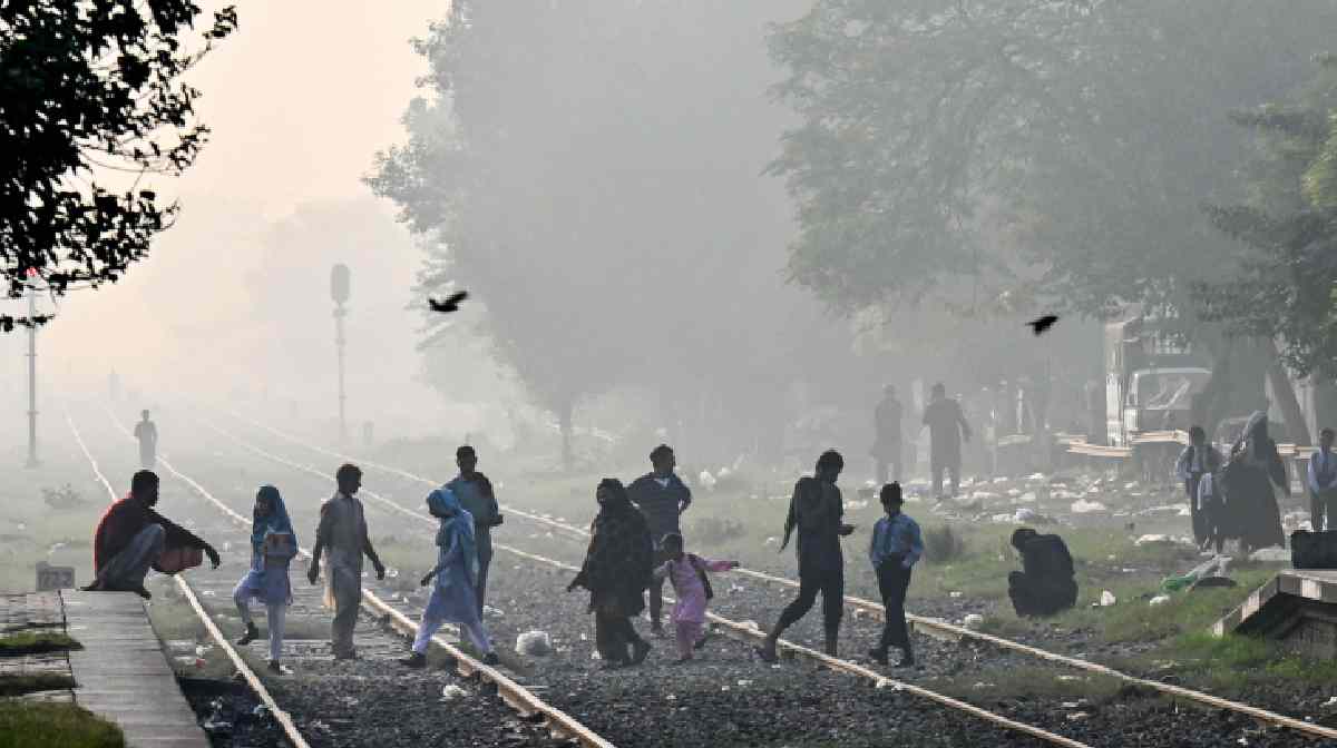 People walk across railway tracks strewn with garbage, amid smoggy conditions in Lahore on November 4, 2024. Air pollution in Pakistan's second biggest city Lahore soared on November 2, with an official calling it a record high for the smog-choked mega city. (Photo by Arif ALI / AFP)