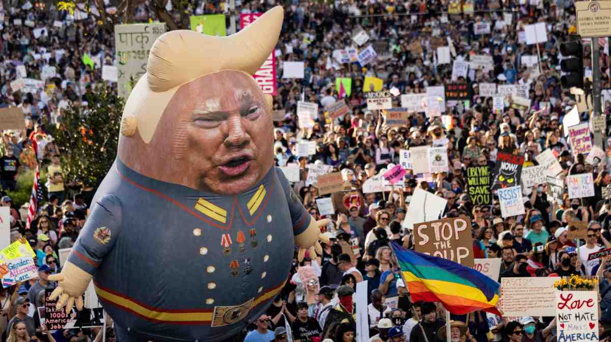A large balloon with an image of US President Donald Trump is seen above protesters holding signs during the nationwide "Hands Off!" protest against Trump and his advisor, Tesla CEO Elon Musk, in downtown Los Angeles on April 5, 2025. Protesters flooded the streets of several major US cities on Saturday to oppose the divisive policies of President Donald Trump, in the largest demonstrations since his return to the White House. Opponents of the Republican president's policies -- from government staffing cuts to trade tariffs and eroding civil liberties -- rallied in Washington, New York, Houston, Los Angeles and Florida, among other locations. (Photo by ETIENNE LAURENT / AFP)