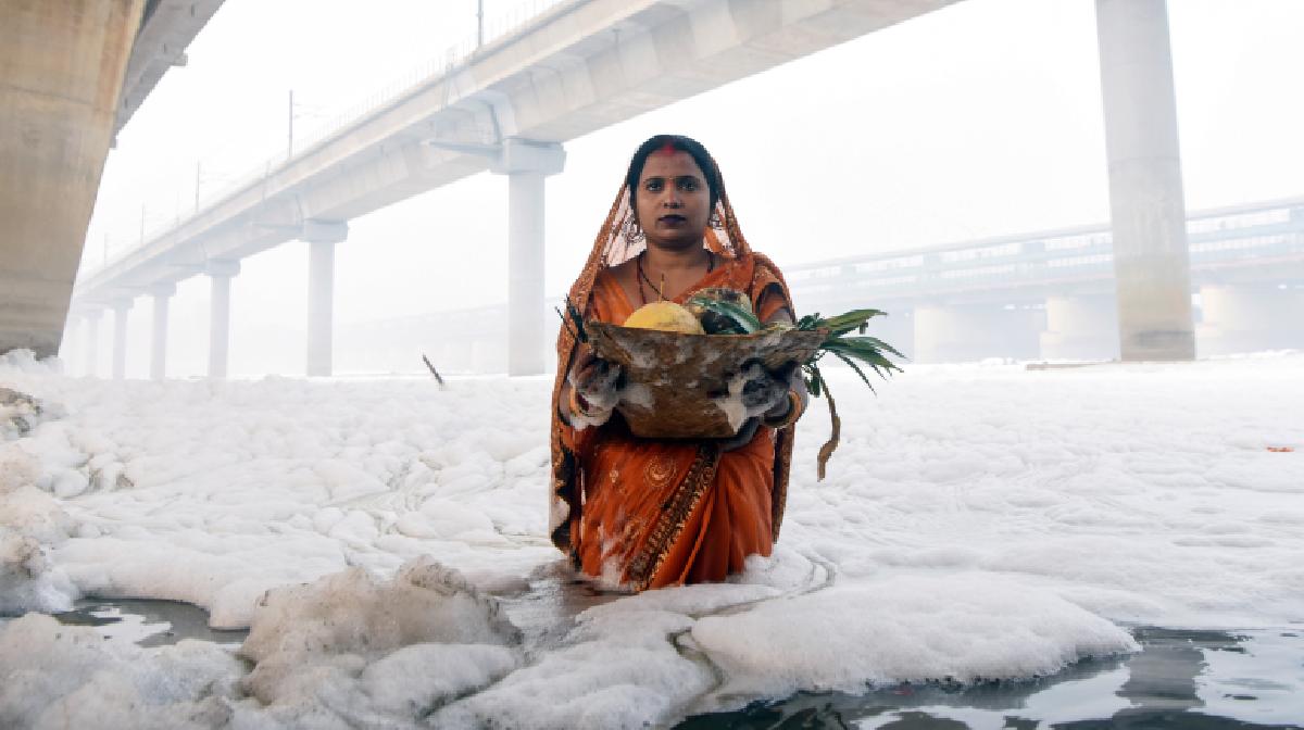 Devotees offer 'Arghya' to the rising Sun amid toxic foam-laden Yamuna River on the last day of Chhath Puja, at Kalindi Kunj in Noida on Friday. (ANI Photo/Ritik Jain)