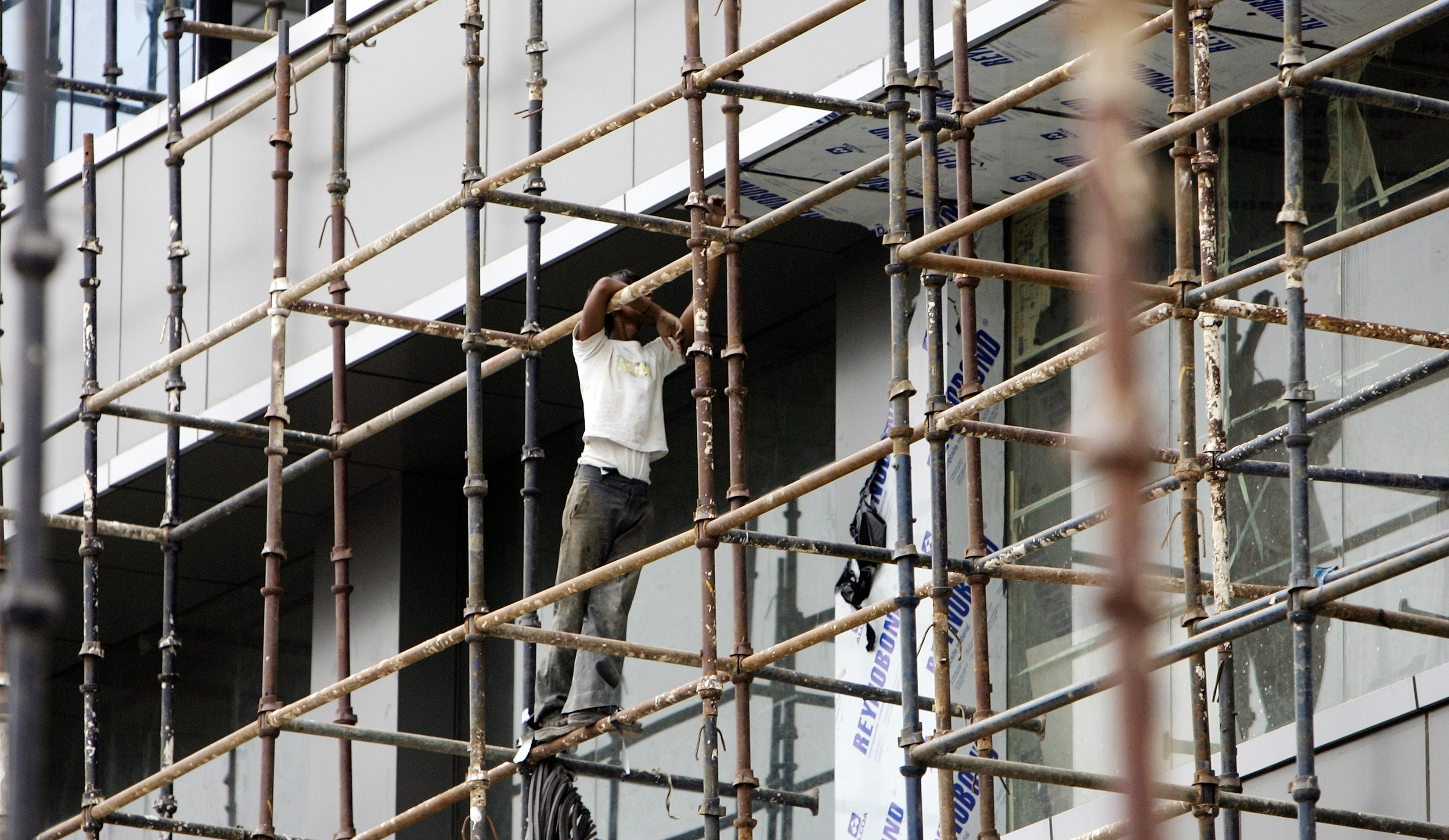 An Indian construction worker clings on to a pole as he goes about his work at an under-construction building in New Delhi, 25 May 2007. India has unveiled an ambitious plan to provide old-age and health protection to the country's estimated 370 million casual workers for the first time, officials said Friday.      AFP PHOTO/ MANAN VATSYAYANA